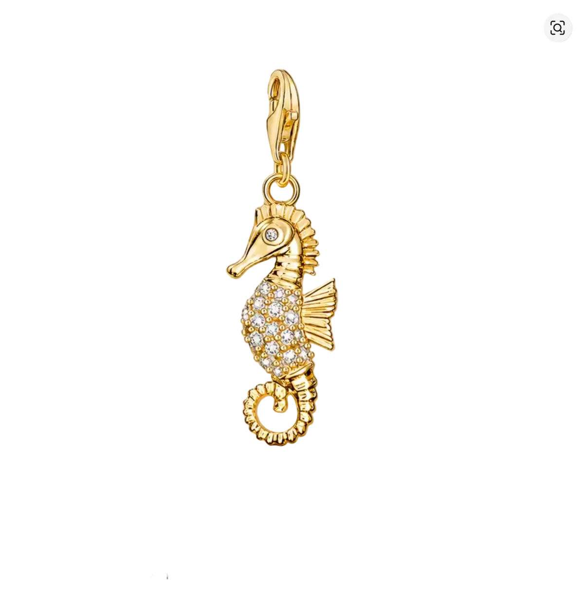 A gold seahorse-shaped charm or pendant with a small clear stone eye and a body paved with clear rhinestones, hanging against draped champagne satin fabric. The word THADDAEUS appears below, with smaller text 'CREATE YOUR OWN STYLE'.