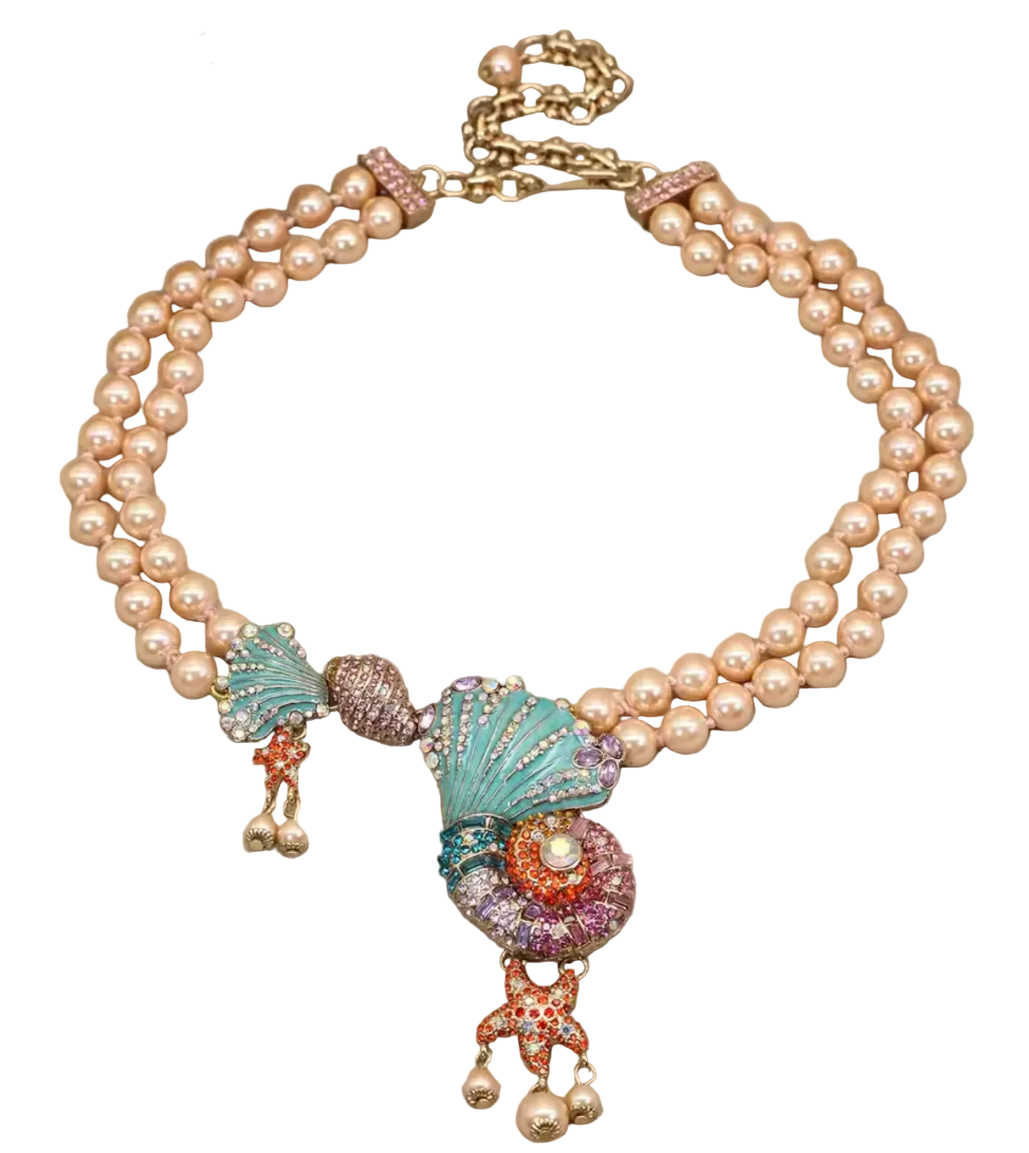 A double-strand pearl necklace with a colorful shell and starfish pendant, embellished with gold-tone chain and rhinestone details, displayed on a neutral beige surface with decorative flowers in the corner.
