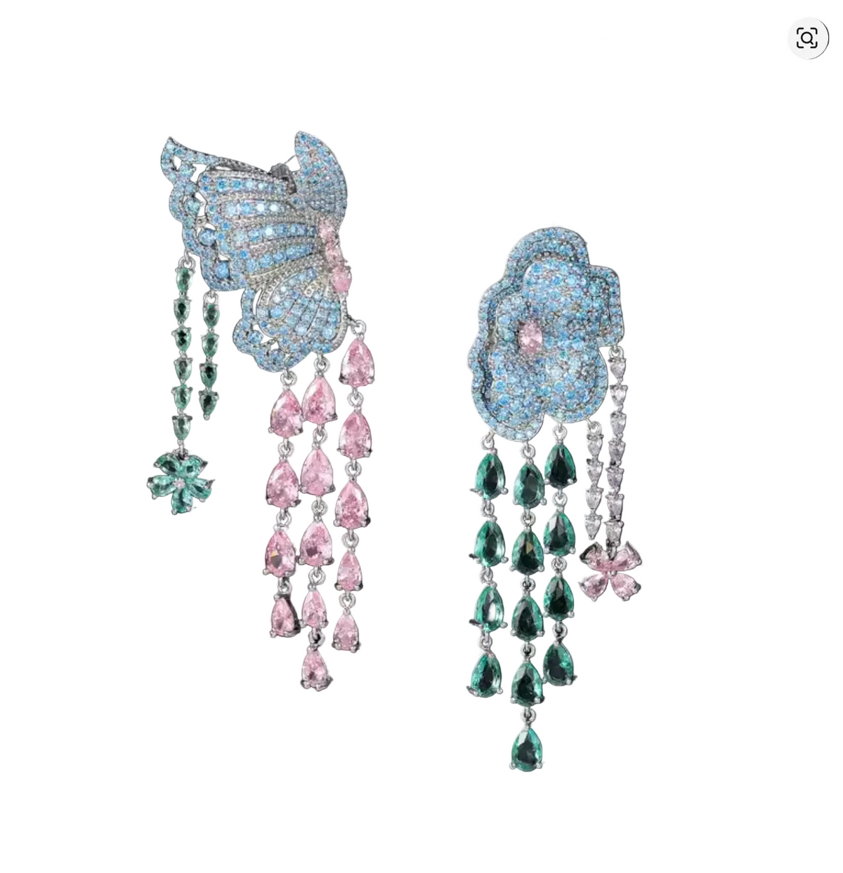 A pair of elaborate dangling earrings on black hair clips against a dark background with warm bokeh lights. The earrings feature light blue pavé butterfly and flower motifs with dangling chains of pink and green teardrop gemstones in silver settings.
