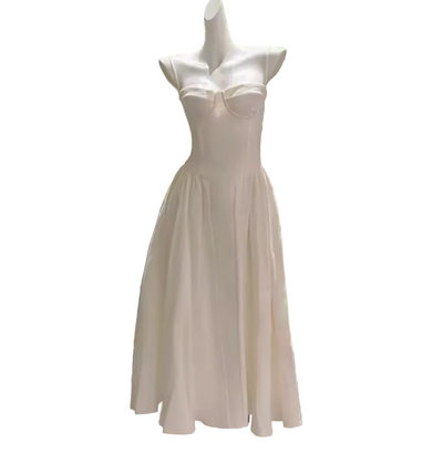 A white sleeveless midi dress displayed on a mannequin indoors, with a structured sweetheart bodice, fitted waist, and flared skirt. The mannequin stands in front of a modern glass-paneled wall and a large potted tree.