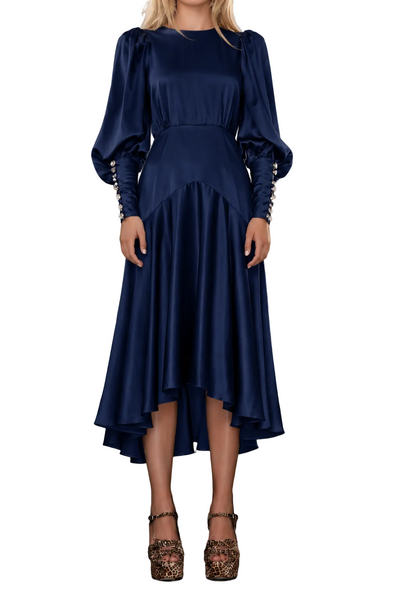 A woman wearing a navy blue satin midi dress with puffed balloon sleeves and beaded cuffs, standing on stone stairs.