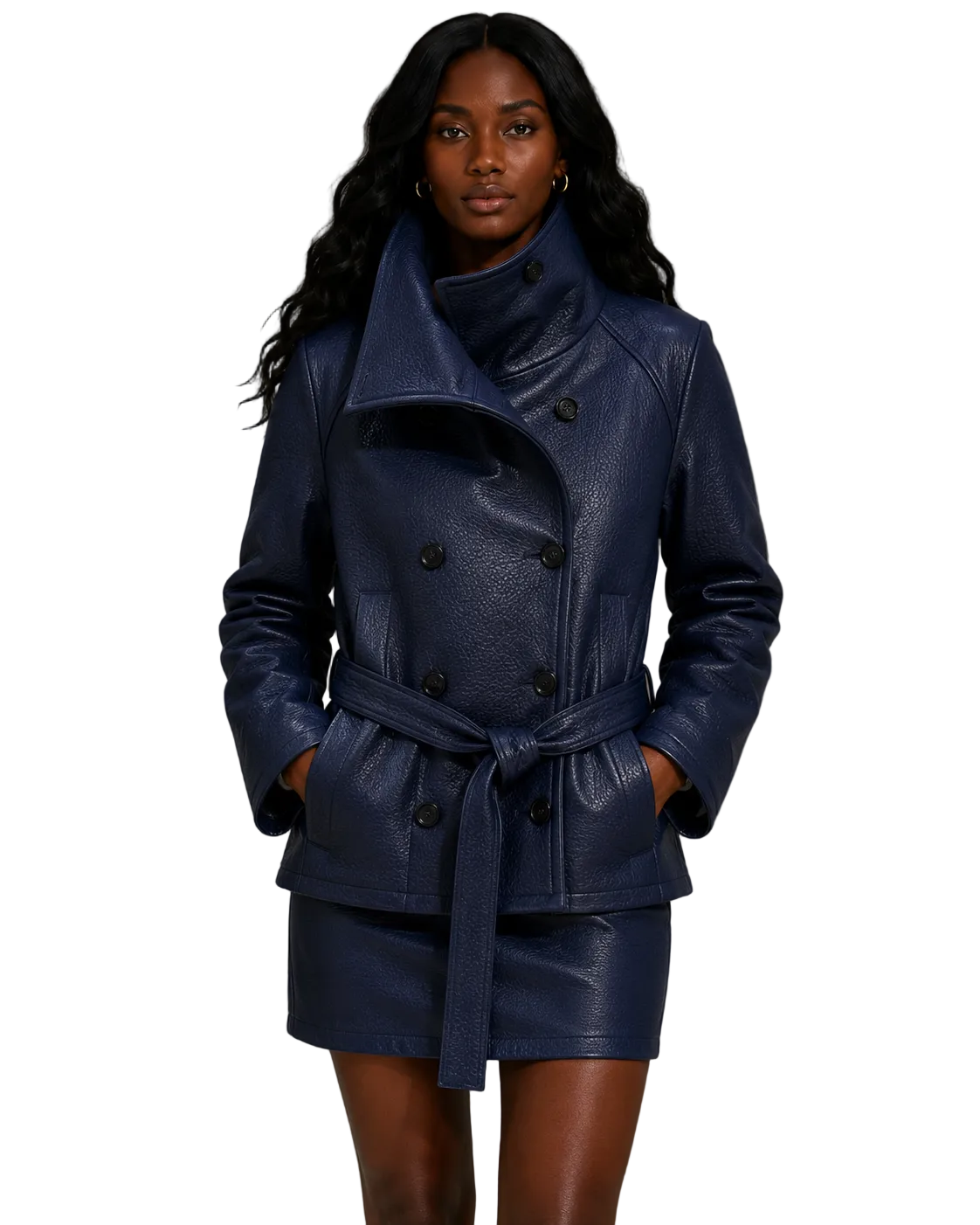 A woman modeling a dark blue textured leather double-breasted wrap coat with a matching belt and matching mini skirt, set against a gray concrete wall.