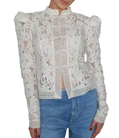 A woman wearing a white floral lace long-sleeve blouse with puffed shoulders and a high collar, paired with light blue jeans, shown from the neck down against a plain light gray background.